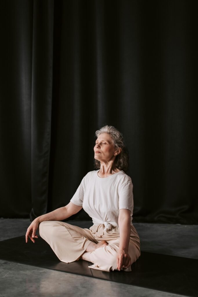 Senior woman sitting in meditation pose indoors on a yoga mat, embracing mindfulness and tranquility.